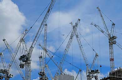 A skyline filled with many cranes, with a blue sky background with white clouds